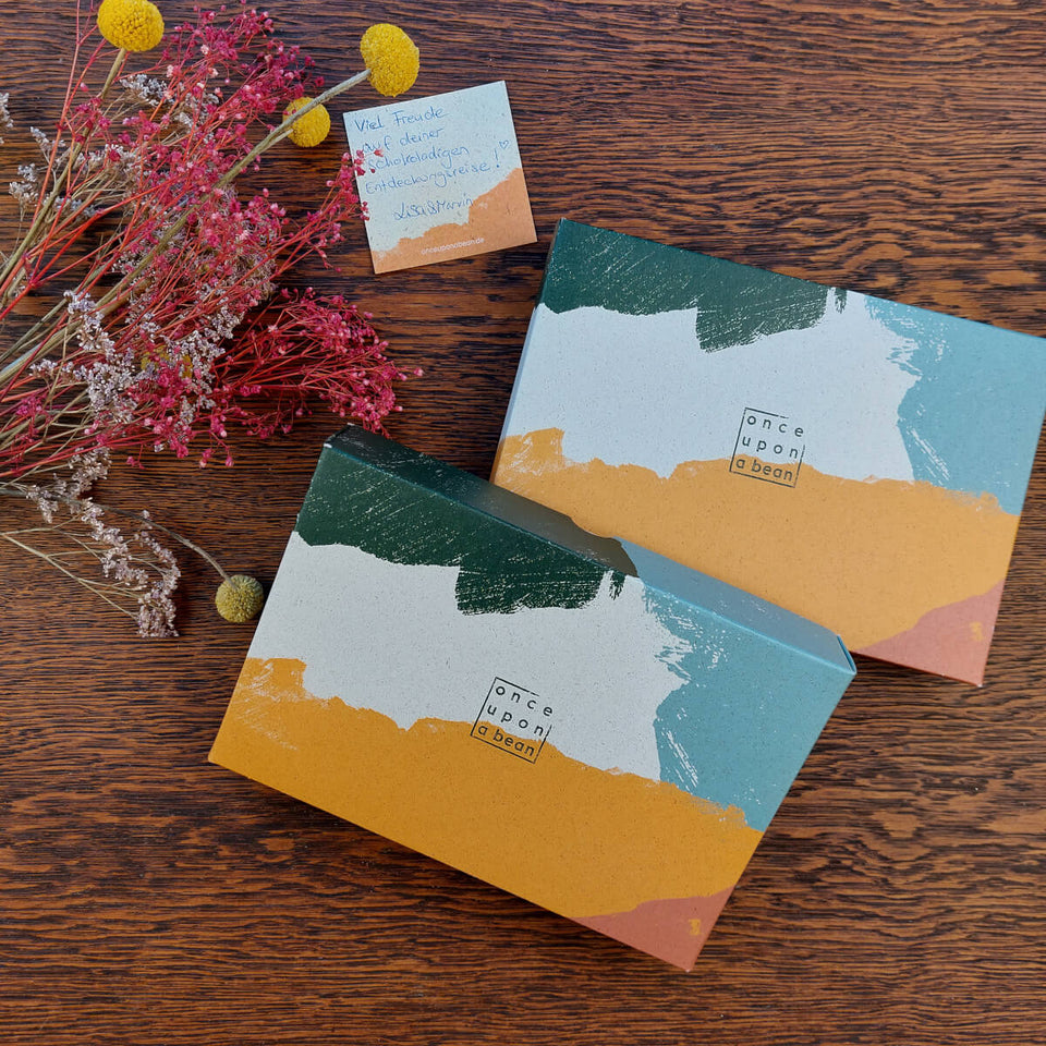 Zwei farbenfrohe Schoko Geschenkboxen mit Grußkarte und Blumen